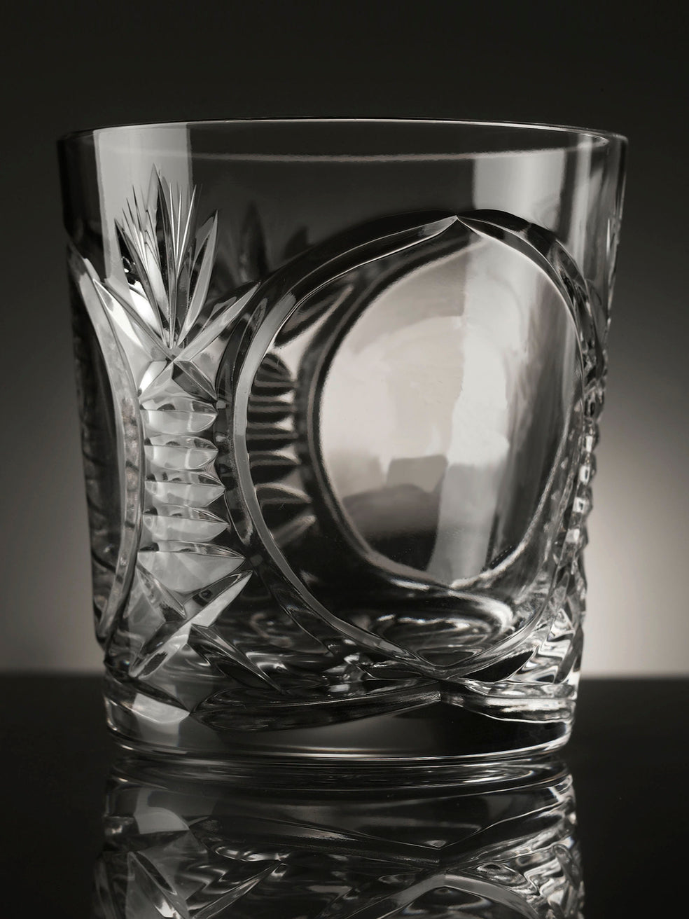 Cut crystal glass tumbler with intricate designs on a reflective surface