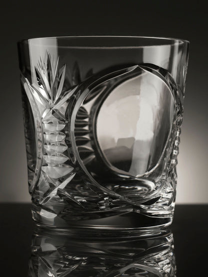 Cut crystal glass tumbler with intricate designs on a reflective surface
