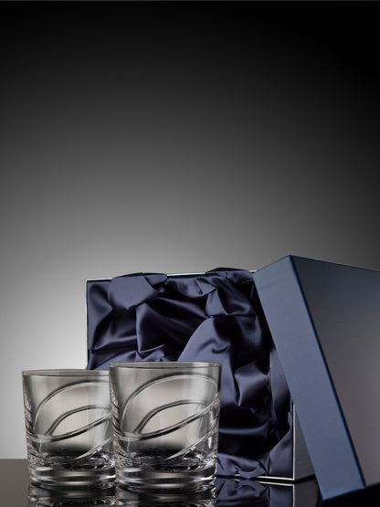 Two clear glass tumblers with a decorative pattern on a dark gray background with a blue satin box.